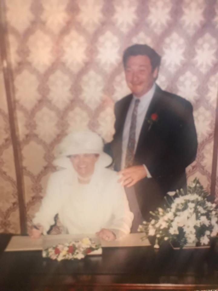 Image of woman at a wedding signing the register with man standing behind her. 