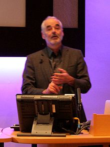 Professor Spiegelhalter standing behind a lecturn giving a presentation of The Uncertainty of Coincidence